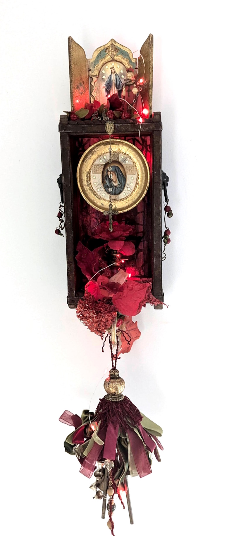 An assemblage sculpture titled 'She Shines Radiant Red,' featuring vibrant red hues and LED lights that create an ethereal glow. The artwork portrays Mary as a spiritual vessel, symbolizing her faith illuminated through art.