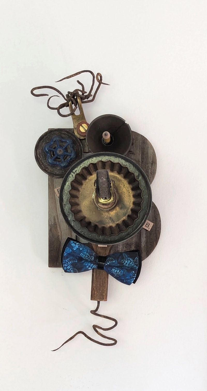 Boring Bob, a whimsical pencil holder made from found materials during my assemblage workshop experience, featuring a blue water spigot eyeball, rusted wire hair, and a blue tortoise bowtie.