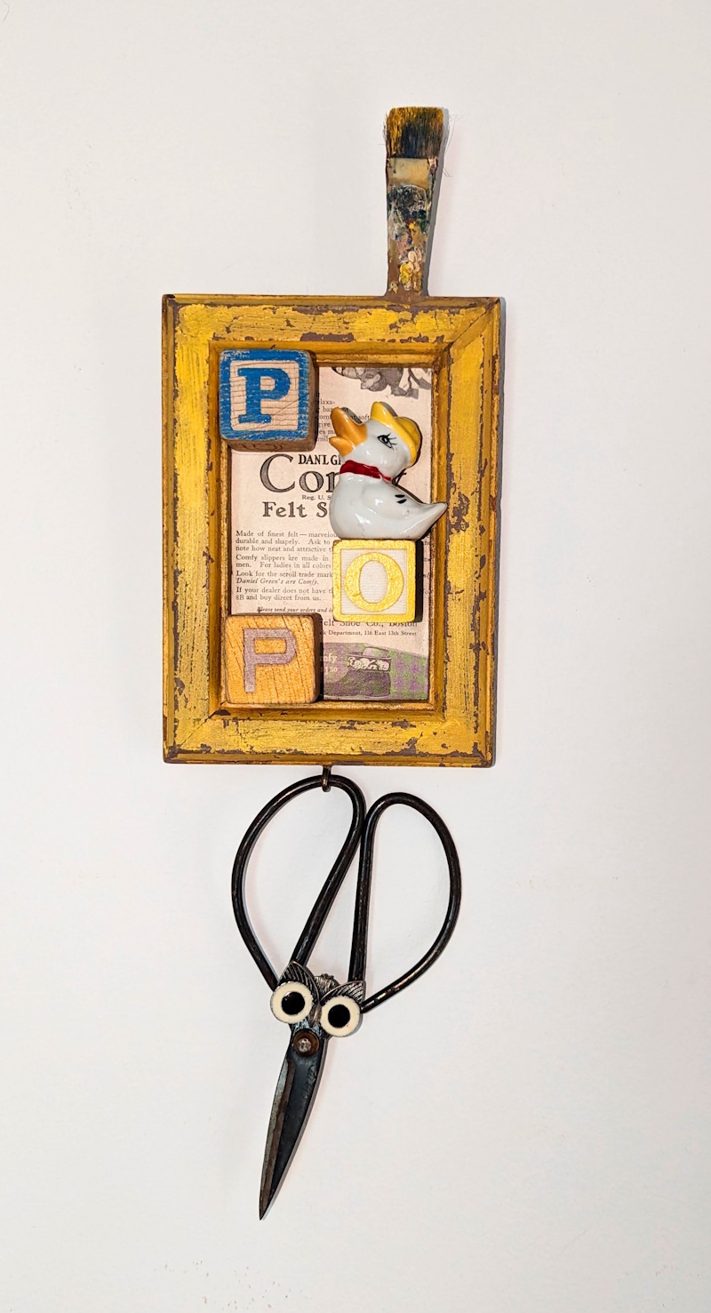 Assemblage artwork featuring a yellow wooden frame with vintage blocks spelling “Pop,” a ceramic duck, a paintbrush, and whimsical scissors with eyes.