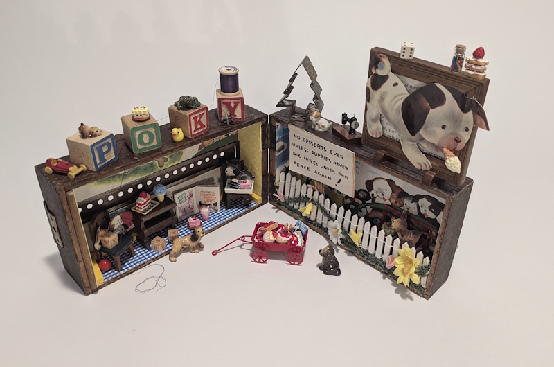 Whimsical mixed media assemblage featuring miniature dogs, toys, blocks spelling “POKY,” tiny desserts, and dollhouse-like scenes arranged around a playful storybook-inspired environment.
